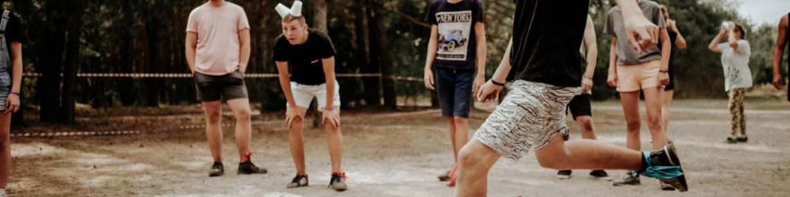 Group of teenagers wearing masks playing a soccer game in a sandy outdoor setting.